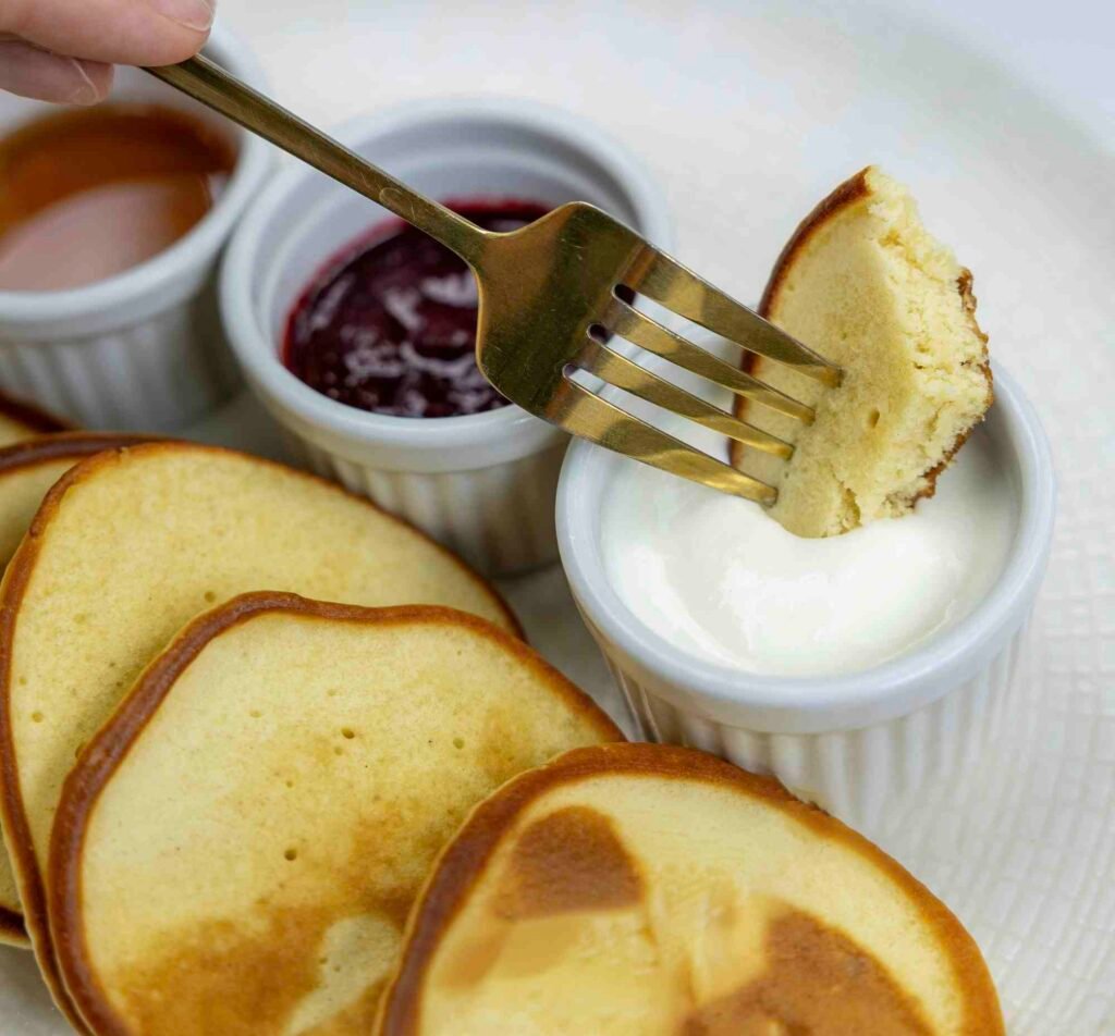 Fluffy pancakes being dipped in a dairy-free alternative to heavy cream with fruit sauces on the side.