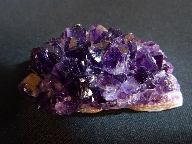 A natural cluster of deep purple Amethyst crystals with sharp geometric points resting on a black background.